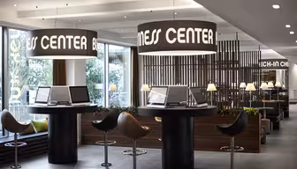 Moderne businesscenter med slanke computerstationer, høje taburetter og store, oplyste cirkulære skilte. Rummet har et moderne design med planter og ambient belysning, der tilbyder en professionel og imødekommende atmosfære.