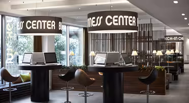 Moderne businesscenter med slanke computerstationer, høje taburetter og store, oplyste cirkulære skilte. Rummet har et moderne design med planter og ambient belysning, der tilbyder en professionel og imødekommende atmosfære.