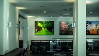 En moderne, minimalistisk cafe med sorte borde og stole, med vægkunst af natur og bybilleder. Indretningen omfatter blød belysning og en ren, neutral farvepalet. Stemningen er rolig og indbydende.