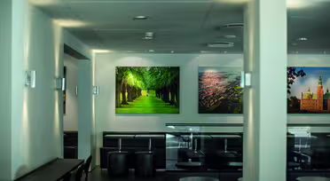 En moderne, minimalistisk cafe med sorte borde og stole, med vægkunst af natur og bybilleder. Indretningen omfatter blød belysning og en ren, neutral farvepalet. Stemningen er rolig og indbydende.